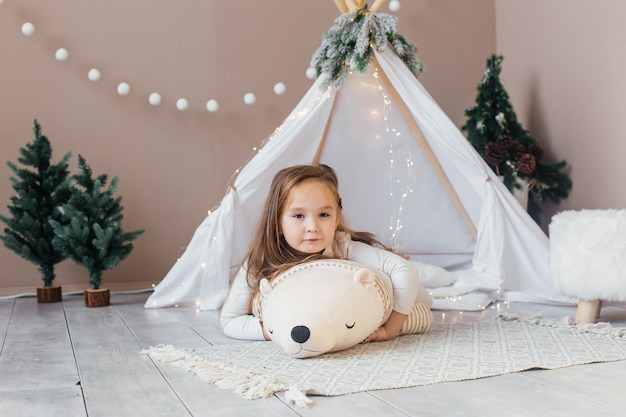 Foto una bambina bellissima in pigiama bianco gioca con un orsacchiotto vicino alla stanza dei bambini del teepee con ca