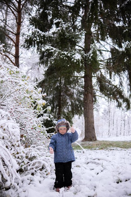 Little beautiful girl in winter clothes standing alone in the middle of a snowy forest