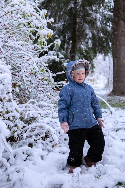 Little beautiful girl in winter clothes standing alone in the middle of a snowy forest