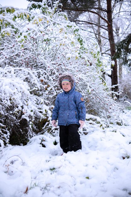 Little beautiful girl in winter clothes standing alone in the middle of a snowy forest