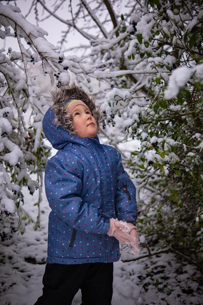 Little beautiful girl in winter clothes standing alone in the middle of a snowy forest