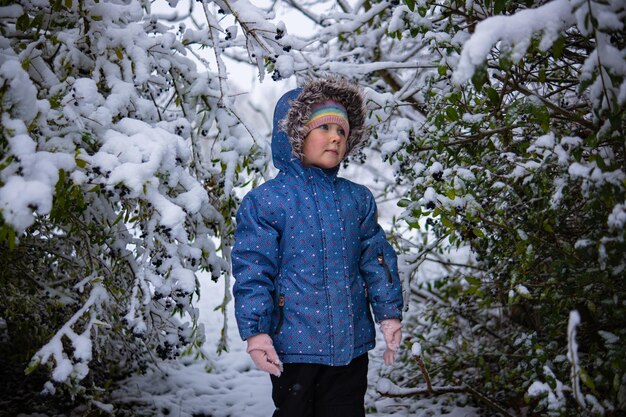 Little beautiful girl in winter clothes standing alone in the middle of a snowy forest