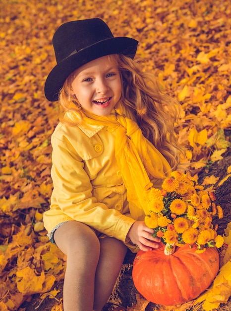 Little beautiful girl with blond hair with big pumpkin in autumn background. Halloween