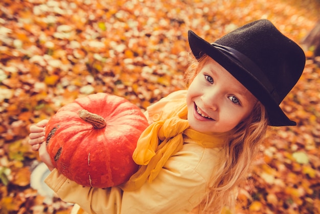 Little beautiful girl with blond hair with big pumpkin in autumn. Halloween