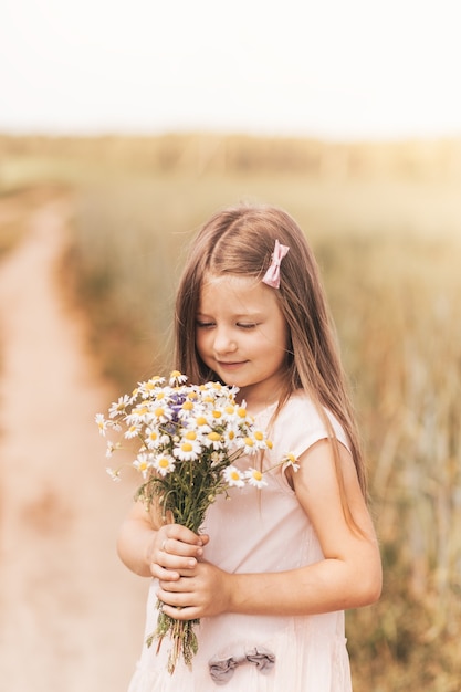 A little beautiful girl with a bouquet of daisies in a wheat field