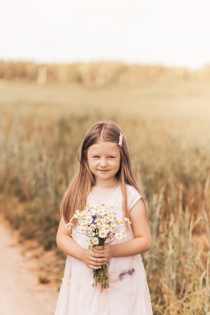 A little beautiful girl with a bouquet of daisies in a wheat field