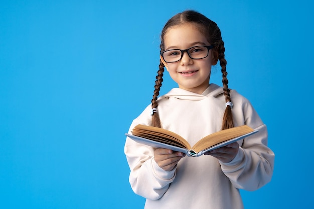 Piccola bella ragazza sorridente che tiene libro su sfondo blu