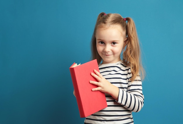 Little beautiful smiling girl holding book on blue background going to school