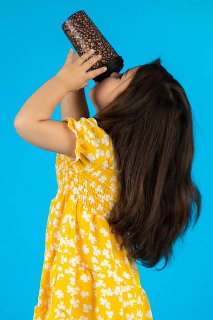 Little beautiful smiling girl with a funny face in a striped yellow dress posing on a blue background in studio