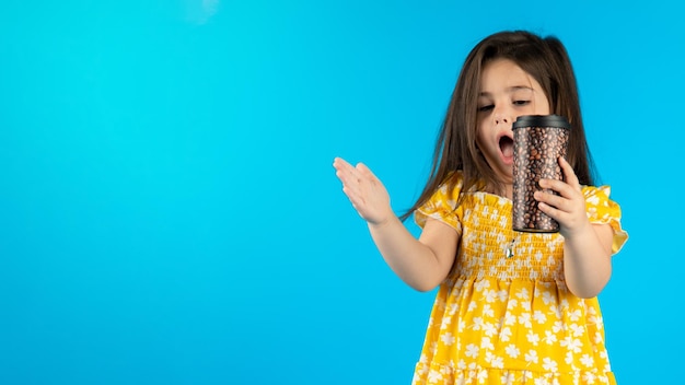 Little beautiful smiling girl with a funny face in a striped yellow dress posing on a blue background in studio