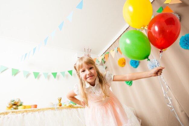 Piccola ragazza di compleanno con corona sulla testa che tiene palloncini colorati. la ragazza principessa alla festa di compleanno