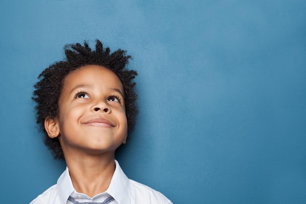 Photo little black child boy smiling and looking up on blue background