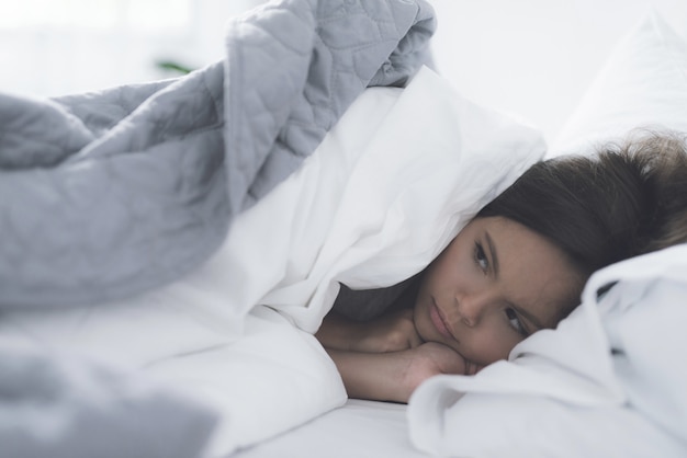 Photo a little black girl lies in a white bed under a white blanket