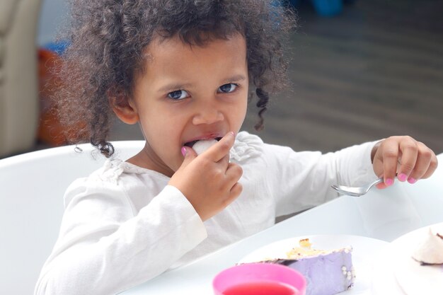 ケーキを食べる小さな黒い笑顔の女の子。デザートフード