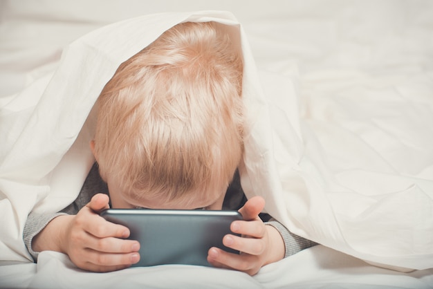 Little blond boy buried his nose in his smartphone. 