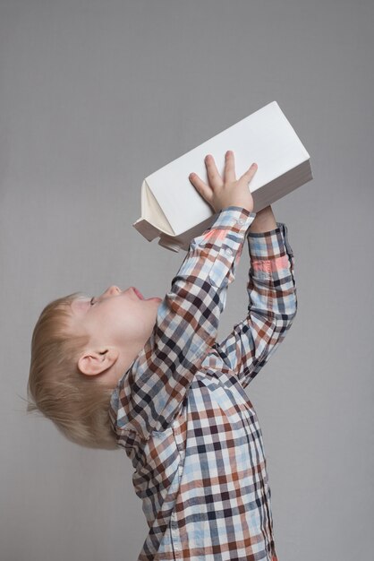 Little blond boy drinks from a large white package