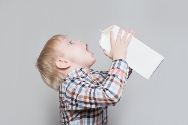 Little blond boy drinks from a large white package.