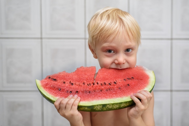 Little blond boy eating a slice of watermelon