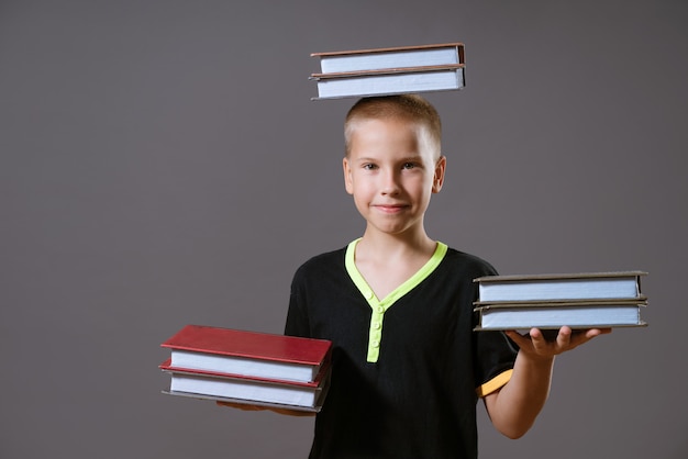 Фото Маленький белокурый мальчик в черной футболке держит в руках стопки книг, а на голове ребенок ...