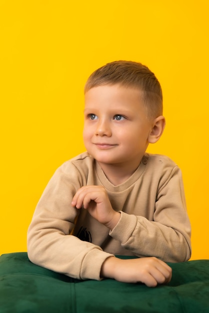 A little blond boy is looking at a space on a yellow background