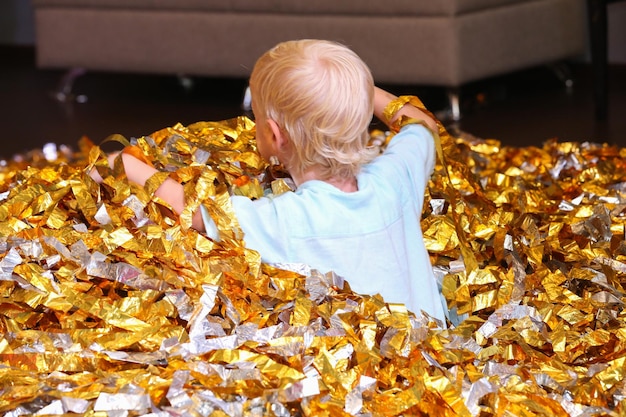 小さな金髪の少年がスライスされた金色の紙の山に座っています
