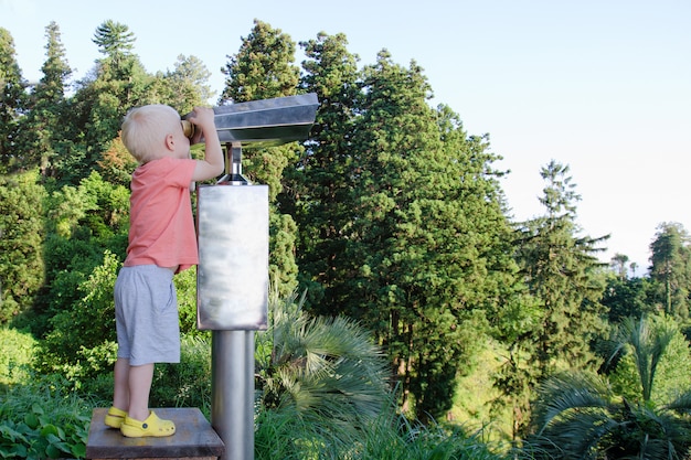 Little blond boy looking in a large pair of binoculars