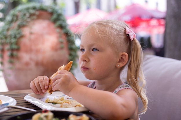 Little blond child eats in a summer cafe. Real people.