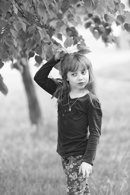 Little blond girl on background of green tree leaves