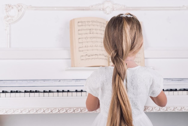 Little blond girl play on white piano in white dress