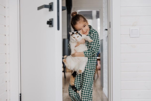 A little blond girl wearing pajamas hugs a domestic cat in her bedroom The concept of a cozy home morning