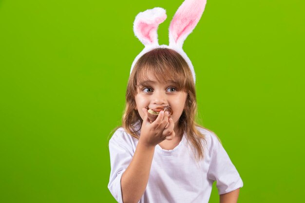 Little blond girl with dirty chocolate bunny ears eating Easter egg