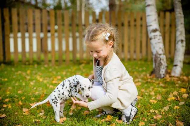 A little blond girl with her pet dog outdooors in parkcute little girl is playing with her puppy in