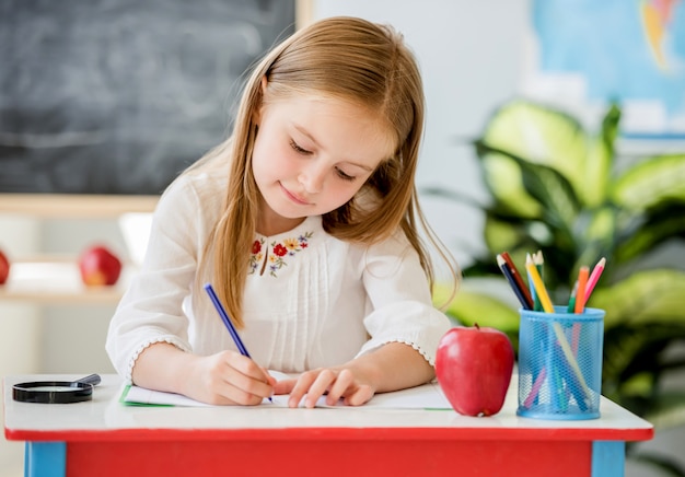 学校の教室で授業を書く小さなブロンドの女の子