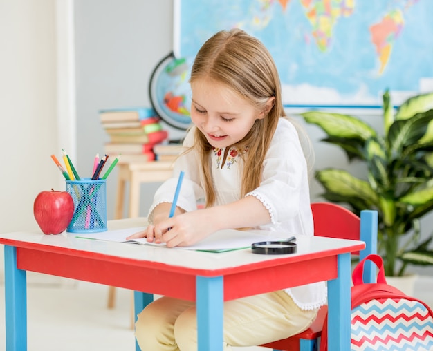 Little blond girl writing classwork in the school classroom