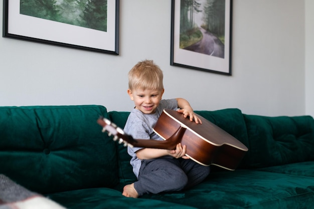 집에서 기타를 연주하는 작은 금발 머리 아이