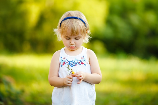 Bambina bionda di 2-3 anni che gioca nel parco estivo e fiori profumati. concetto di attività per bambini