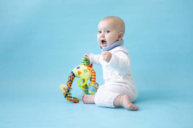 Piccola neonata bionda con un giocattolo in mano in un maglione lavorato a maglia su sfondo blu isolare lo spazio per il testo bambino bambino in abiti invernali inverno