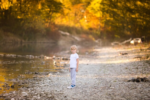 Little blonde boy in green glasses playing on the riverside