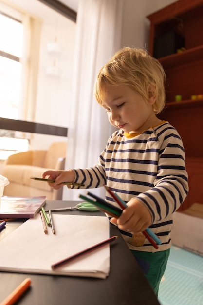 A little blonde boy playing with color pencils