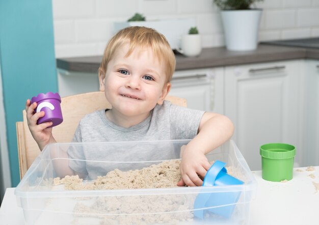 Little blonde boy playing with kinetic sand at home. 