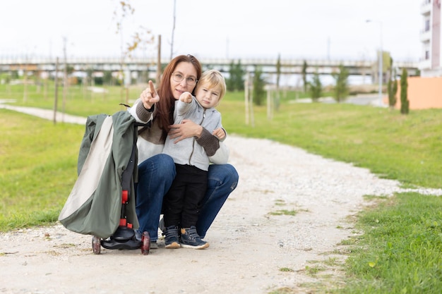 A little blonde boy on walk with his mother  pointing forwards with their fingers