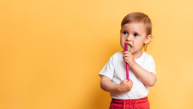 A little blonde girl brushes her teeth with toothpaste. Yellow background. A place for your text. The concept of dental hygiene.
