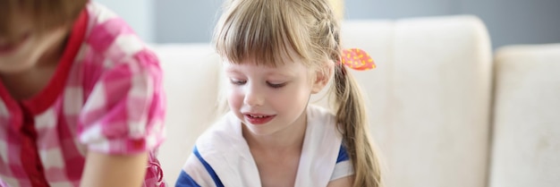 Little blonde girl busy with playing card game on table at home