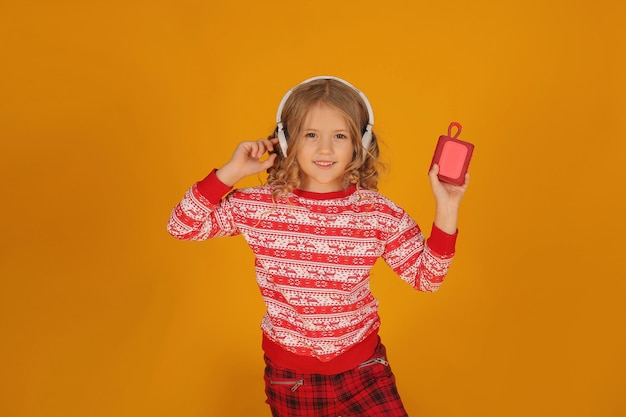 a little blonde girl in a Christmas jumper and plaid trousers listens to music with headphones