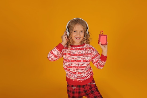 a little blonde girl in a Christmas jumper and plaid trousers listens to music with headphones