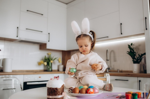 Little blonde girl coloring eggs for Easter holiday at home