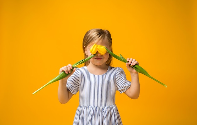 A little blonde girl covered her eyes with tulips on yellow