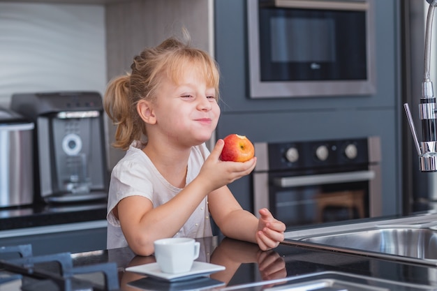 台所でリンゴを食べる小さなブロンドの女の子