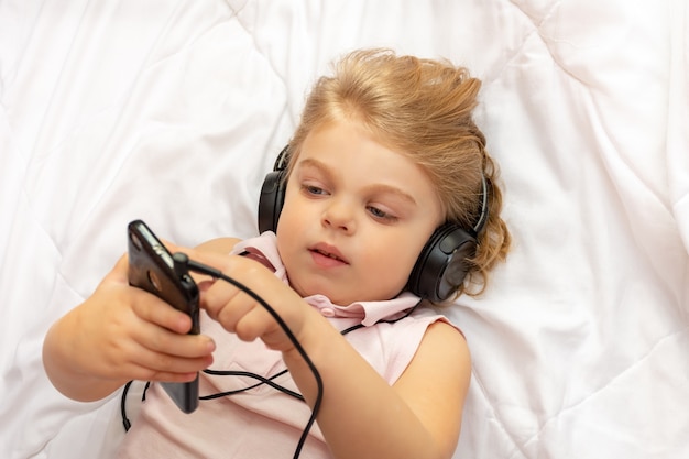 Little blonde girl in headphones listens to music