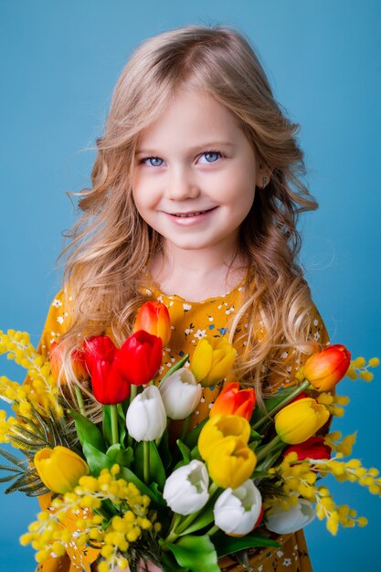 スタジオで青い背景にチューリップの花束を保持している小さなブロンドの女の子